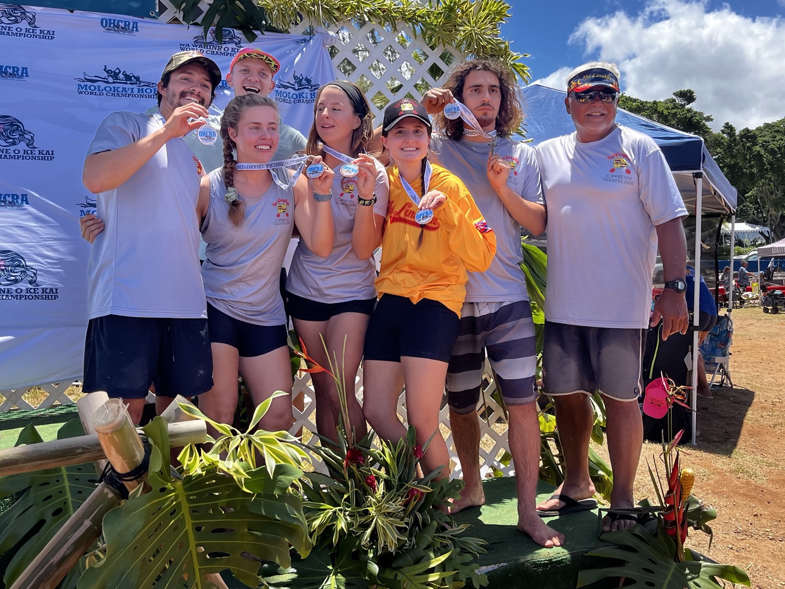 The Hui Lanakila Novice B crew on the awards podium at the 2026 regatta, holding up their medals in front of race banners